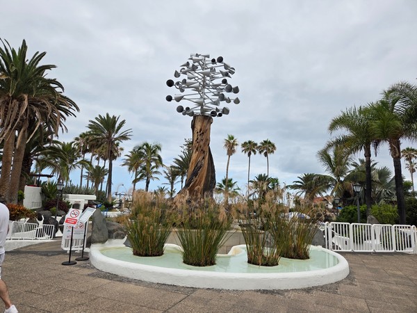 Escultura moderna en el Lago Martiánez de Puerto de la Cruz, rodeada de palmeras, vegetación tropical y un estanque decorativo.