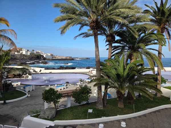 Piscinas del Lago Martiánez en Puerto de la Cruz, con palmeras, solárium y el océano Atlántico al fondo en un día despejado.