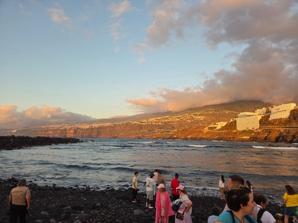 Atardecer en la playa de Martiánez con vistas hacia los acantilados y el Teide parcialmente cubierto por nubes.