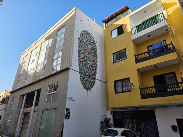 Mural de arte urbano en Puerto de la Cruz pintado en la fachada de un edificio, con una figura abstracta multicolor que destaca entre construcciones residenciales.
