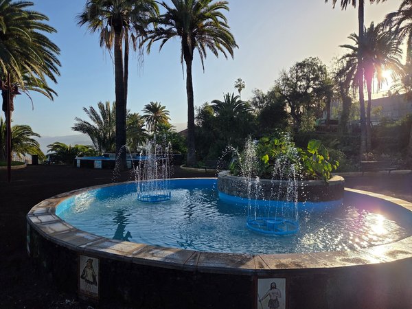 Fuente circular del Parque Taoro en Puerto de la Cruz, rodeada de palmeras y vegetación tropical con chorros de agua en funcionamiento.