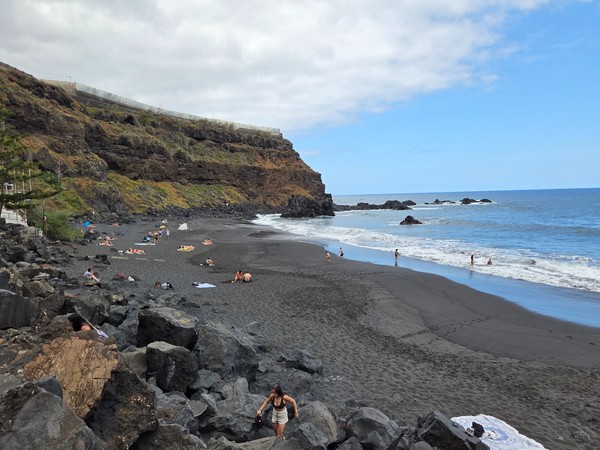 Playa del Bollullo en La Orotava con arena negra, acantilados volcánicos y bañistas disfrutando del mar.
