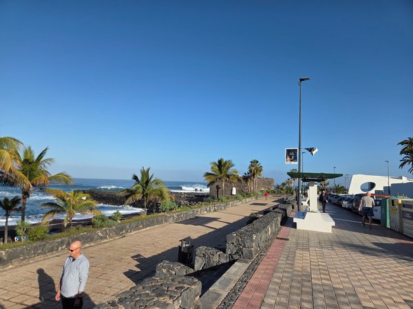 Paseo marítimo de Playa Jardín en Puerto de la Cruz, con palmeras, muros de piedra volcánica y el océano Atlántico al fondo en un día soleado.