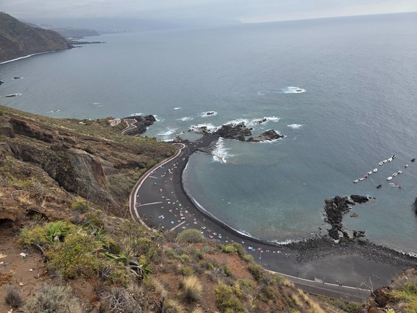 Vista panorámica de playa de Mesa del Mar con su arena negra y acantilados verdes al fondo.