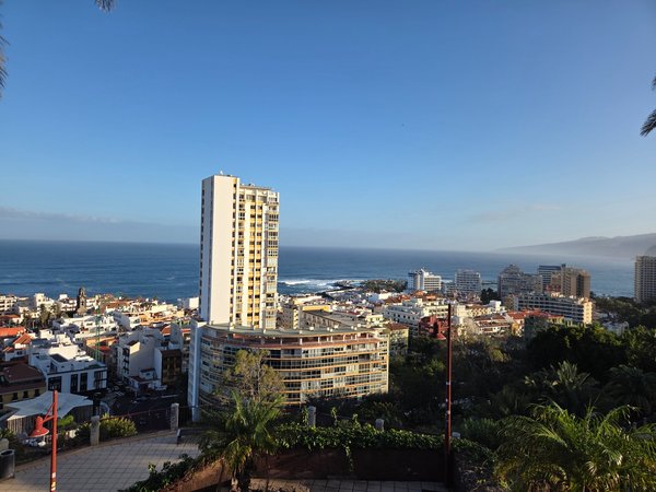 Vista panorámica desde Taoro hacia Puerto de la Cruz, con edificios altos, el casco urbano, el océano Atlántico y la costa al fondo bajo cielo despejado.