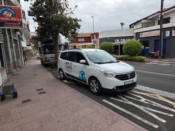 Taxi estacionado en Puerto de la Cruz frente a locales y restaurantes en una calle tranquila.